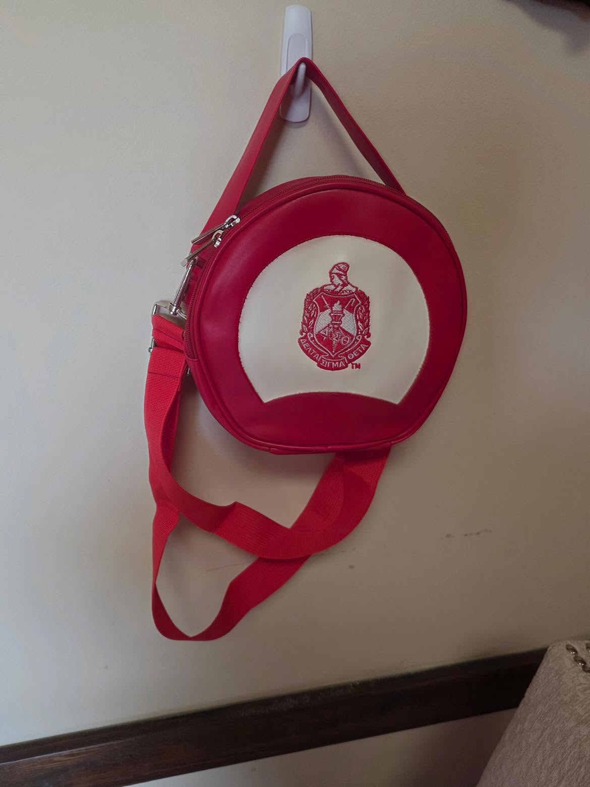 Red circular canteen crossbody bag with cream face and embroidered Delta crest