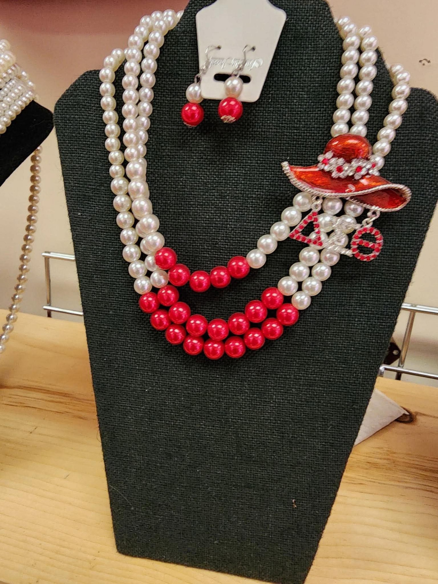 Layered white and red pearl necklace set with Delta hat brooch and matching pearl earrings on a display bust
