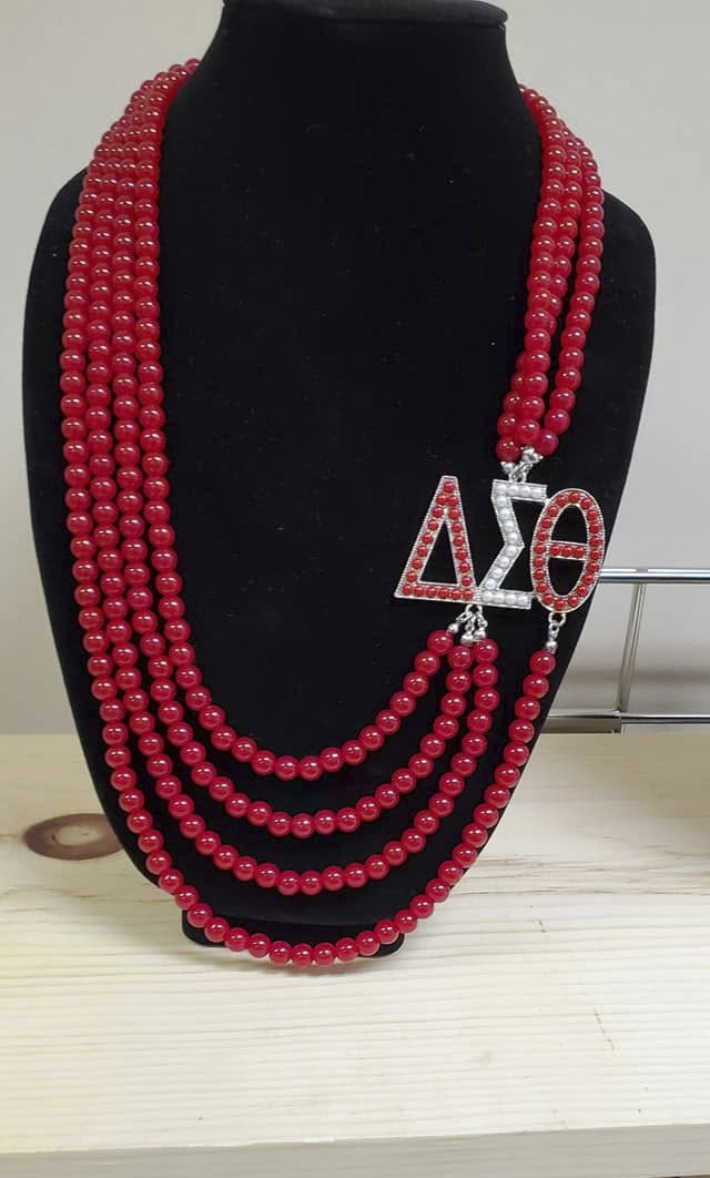 Layered crimson bead necklace with a crystal ΔΣΘ pendant on a black display bust