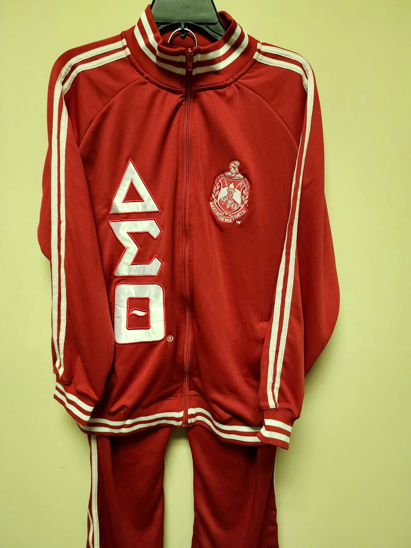 Red Delta Sigma Theta jogging suit with white satin Greek letters and striped trim on a hanger