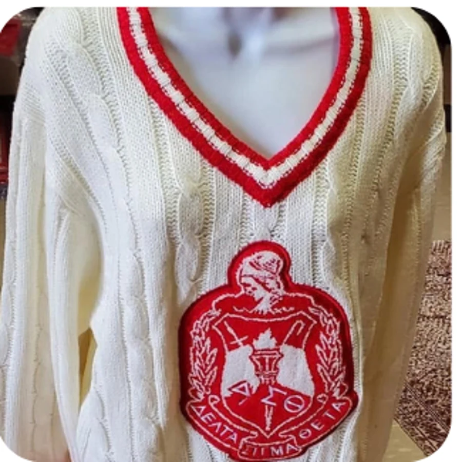 Ivory cable-knit V-neck sweater with red varsity trim and oversized crest