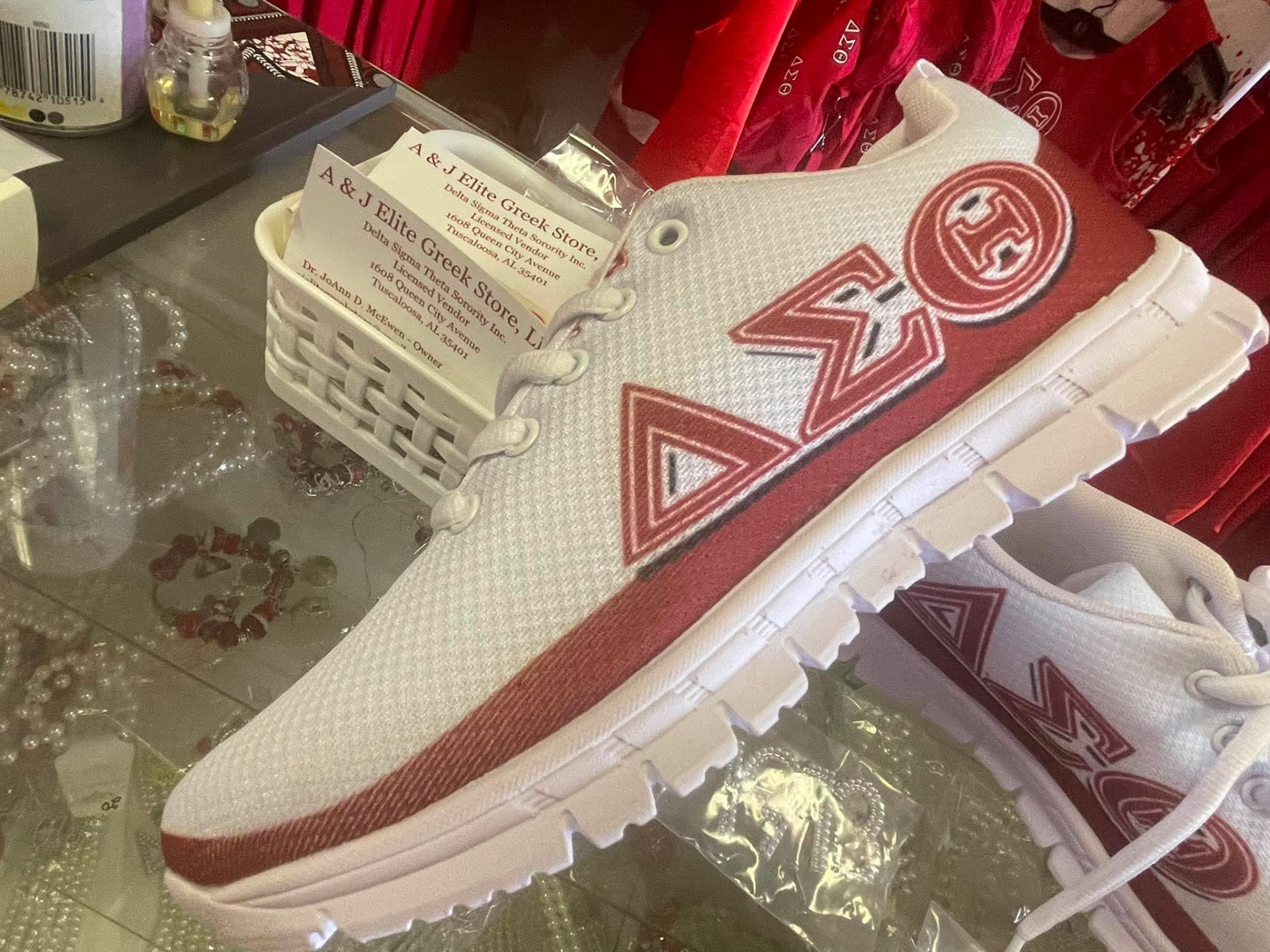 White and crimson Delta Sigma Theta sneakers with Greek letters displayed in the A & J Elite Greek Store case